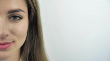 Beyaz arka planda kameraya dik dik bakan genç, beyaz tenli, beyaz bir kadının yarım yüz çekimi.