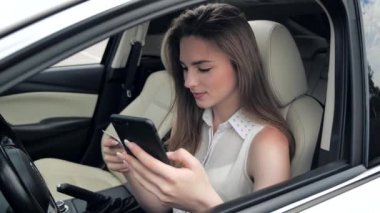 Arabada oturan, elinde kredi kartı ve akıllı telefonuyla gülümseyen genç kız müşteri. İnternetten alışveriş yapan mutlu bayan alışverişçi kolay taşınabilir ödemeler yapıyor. E-bankacılık uygulama servisi