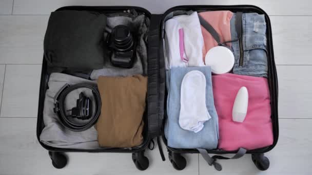 Bovenaanzicht van een koffer waarin vrouwenhanden zetten dingen voor familie vakantie mannen kleding en vrouwen. Vrouwelijke handen met beige manicure te verpakken in een koffer, het uitzicht vanaf de bovenkant — Stockvideo