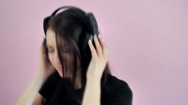 Gülümseyen ve gülen genç kadın siyah kulaklıklarla müzik dinliyor, pembe arka planda dans ediyor.