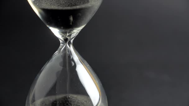 Extreme close up of a transparent hourglass with flowing black sand on blur dial background. Old classic timer. Time concept 4k — Stock Video