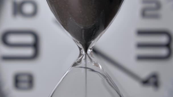 Extrême gros plan d'un sablier transparent avec sable noir coulant sur fond de cadran flou. Ancienne minuterie classique. Concept de temps 4k — Video