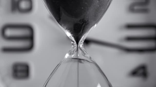 Macro shot sablier transparent avec sable noir coulant sur fond de cadran flou. Ancienne minuterie classique. Concept de temps 4k — Video