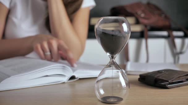 Reloj de arena de primer plano. Silueta mujer leyendo un libro sobre un fondo borroso 4k — Vídeos de Stock