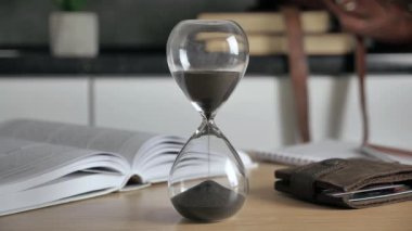 Şeffaf bir mataradaki kum saati, zamanın geçişini noktalayan modern bir iç arka plan dökülür.