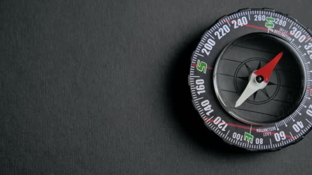 Ein moderner Kompass liegt auf einem schwarzen Schreibtisch mit einem roten Pfeil, der die Richtung anzeigt. Reise-, Abenteuer-, Expeditions-, Geschäfts-, Auswahl- und Möglichkeiten-Konzept. 4k — Stockvideo