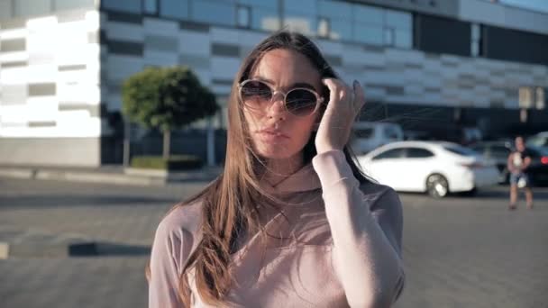 Retrato de hermosa mujer joven con gafas mirando a la cámara en cámara lenta como el viento sopla su pelo 4k — Vídeos de Stock