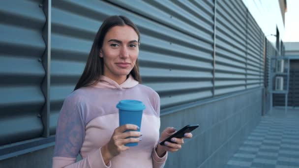 Jovem mulher atraente olhando surpreendente telefone celular conversando, surfando na internet bebendo café e rindo no fundo do centro de negócios. 4k — Vídeo de Stock