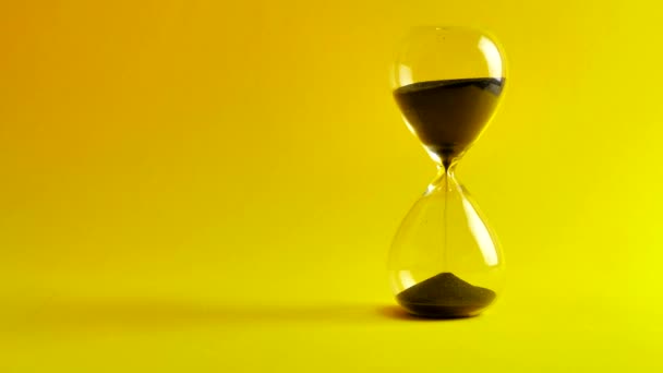 Hourglass Countdown Sand falls in a glass flask on yellow background. passing time. 4k — Stock Video