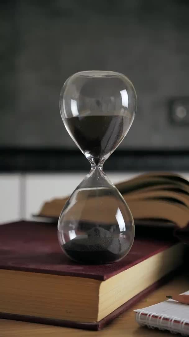 Shot of a sand clock measuring time while the sand is falling down against the black sand on blur modern interior background. Old classic timer. Time concept 4k — Stock Video