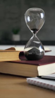 Kum saatinin dikey görüntüsü. Kum, modern arka planda siyah kuma doğru düşerken zamanı ölçüyor. Klasik zamanlayıcı. Zaman kavramı 4k