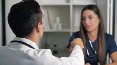 Gülümseyen kadın doktor, erkek doktorun elini sıkar ve anlaşmayı kabul eder. Beyaz üniformalı mutlu doktor, sıhhiye güven konsepti 4k 'de el sıkışıyor.