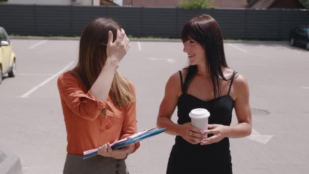 Twee zakenvrouwen die lopen, glimlachen, koffie drinken en roddelen. Lunchpauze concept — Stockvideo