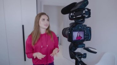 Mutlu genç kadın blogcu evde profesyonel kamerayla video kaydediyor. 4k