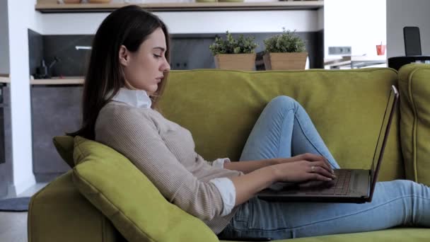 Freelancer mulher séria relaxado usando dispositivo laptop inclinado no sofá em casa escritório, empreendedor focado trabalhando distantemente digitando no notebook no apartamento — Vídeo de Stock