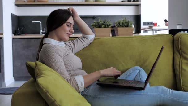 自宅のオフィスでソファにもたれてノートパソコンのデバイスを使用してリラックスした深刻な女性学生,焦点を当てた起業家は遠くアパートでノートパソコンを入力します4k — ストック動画