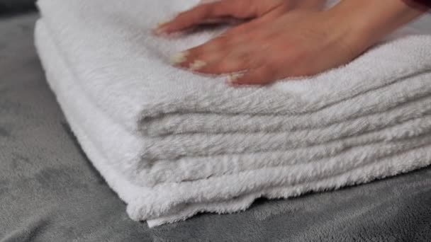 Gros plan des mains mettant une pile de serviettes de bain blanches fraîches sur le drap de lit. — Video