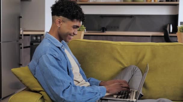 Afrykański wolny strzelec pracujący na komputerze w domu. Nastolatek uśmiechnięty i wpisując tex rozwijający nowy projekt podczas pracy na laptopie w domu. — Wideo stockowe