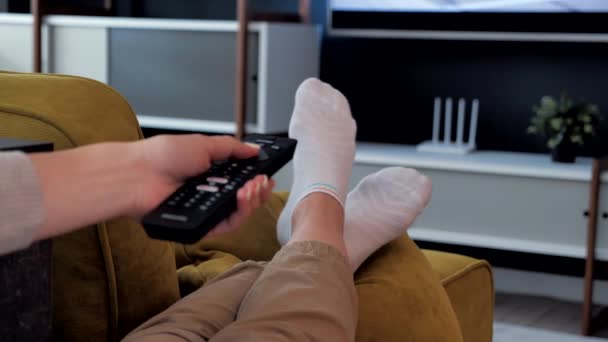 Voeten ontspannen tv kijken op de bank om comfortabel te ontspannen in de woonkamer, sociale afstand en de bescherming van de ziekte Covid 19 concept 4k — Stockvideo