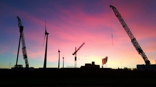 Grúas y molinos de viento girando en la puesta de sol púrpura en otoño — Vídeos de Stock