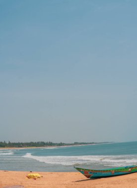 Okyanusun yanındaki sahilde bir tekne oturuyor. Gökyüzü açık ve mavi, ve su sakin