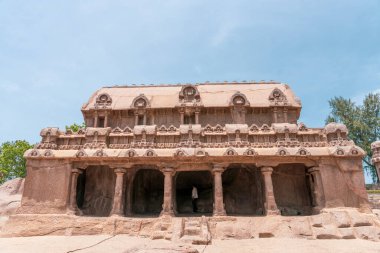 Bir sürü sütunu olan büyük bir bina. Önünde bir insan duruyor. mahabalipuram