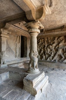 Üzerinde aslan oyması olan taş bir sütun. Sütun taştan bir duvarı ve taş zemini olan bir odada.