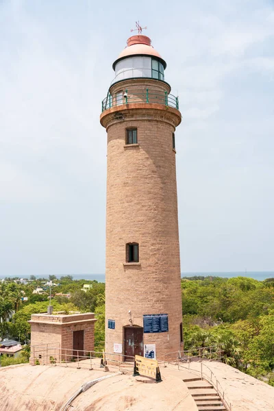 Üzerinde mavi bir işaret olan uzun bir deniz feneri. Deniz feneri bir tepenin üzerinde ve okyanus manzarası var.