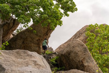 Bir adam kaya duvarına tırmanıyor. Kaya duvarı büyük kayalardan yapılmıştır. Adam yeşil bir gömlek giyiyor. Tamil Nadu.