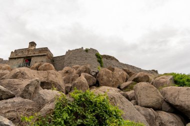 Üstünde küçük bir bina olan büyük bir kaya duvarı. Binanın bir kapısı ve penceresi var. Tamil Nadu.