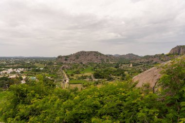 Uzakta bir kasabası olan bir dağ sırası. Dağlar ağaçlarla çevrili. Gökyüzü bulutlu. Tamil Nadu.