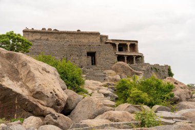 Küçük kapısı olan büyük taştan bir bina. Bina kayalarla çevrili. Gökyüzünde birkaç kuş var. Tamil Nadu.