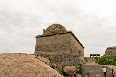 Tepesinde kubbe olan taş bir bina. Bir grup insan basamakları tırmanıyor. Bina bir tepenin üzerinde. Tamil Nadu.