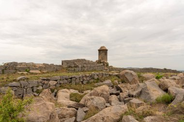 Tepesinde kule olan büyük bir taş bina. Bina kayalarla çevrili. Gökyüzü bulutlu. Tamil Nadu.