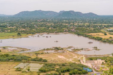 Büyük bir su kütlesi bir çimen tarlası ile çevrilidir. Sahada birkaç kişi var. Tamil Nadu.