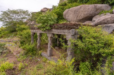 Taştan çatılı taş bir bina. Çatı yosunla kaplı. Bina ağaçlar ve çalılarla çevrili. Tamil Nadu.