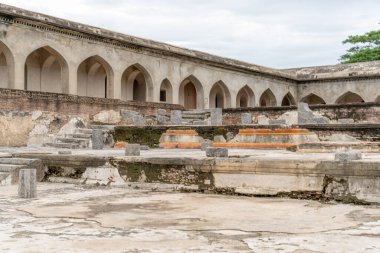 Kemerli pencereleri ve avlusu olan büyük bir bina. Avlu bomboş. Avluda bir kaç bank var. Tamil Nadu.