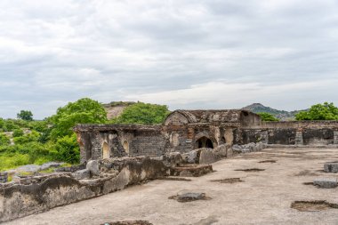 Taş duvarı ve taş çatısı olan büyük bir bina. Çatı kiremitleri kayıp. Bina ağaçlarla çevrili. Tamil Nadu.