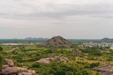 Uzakta bir dağ sırası görülebilir. Gökyüzü bulutlu ve manzara yeşildir. Uzakta bazı evler var. Tamil Nadu.