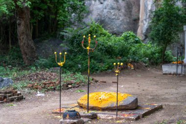 Bir kayanın üzerinde üç tane sarı ve kırmızı mızrak heykeli var. Kaya toprak zeminde. Tamil Nadu.