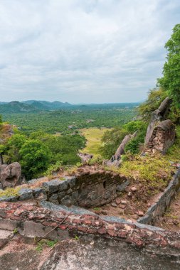 Önünde küçük bir bina olan bir dağ manzarası. Bina taştan yapılmıştır ve taş bir çatısı vardır. Tamil Nadu.