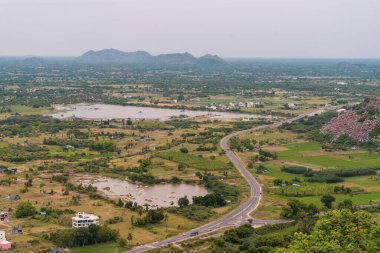 Arka planda göl olan bir yol tarladan geçiyor. Uzakta birkaç ev var. Tamil Nadu.