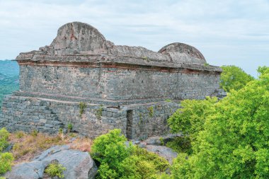 Yeşil çatılı büyük bir taş bina. Çatı yosunla kaplı. Bina ağaçlarla çevrili. Tamil Nadu.