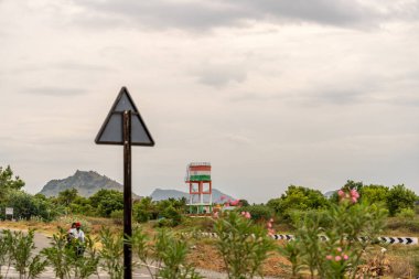 Bir adam yolda motosiklet sürüyor. Yolun kenarında bir tabela var. Tamam mı? Tamil Nadu.