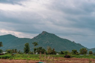 Bulutlu gökyüzü olan bir dağ sırası. Dağlar ağaçlarla çevrili. Dağların arasından geçen bir kablo var. Tamil Nadu.
