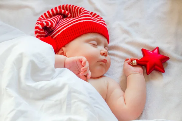 Sleeping cute baby in santa hat waiting for christmas holding red star in hand