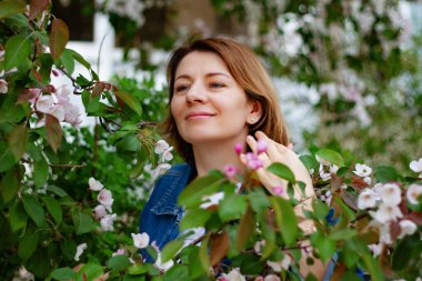 Güzel, kahverengi saçlı, mavi gözlü, elma bahçesinde çiçek kokan bir kadın.