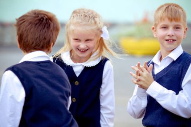Okula dönüş: üç okul çocuğu (erkek ve bir kız) üniforma giyiyorlar ve dışarıda gülüyorlar.