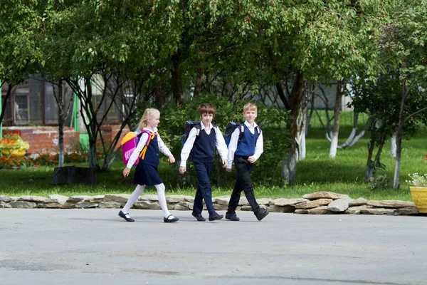 学校に戻る 制服を着た3人の学童 男の子と女の子 が校庭で遊んで笑っている — ストック写真