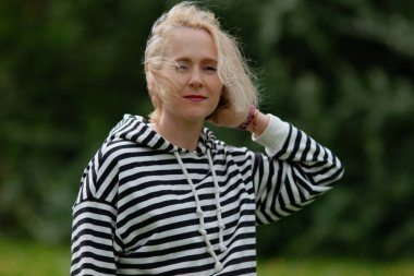 Kırmızı ruj süren güzel sarışın kadın portresi ve açık havada sıradan çizgili kapüşonlu, rüzgarlı saçlı meditasyon havası.